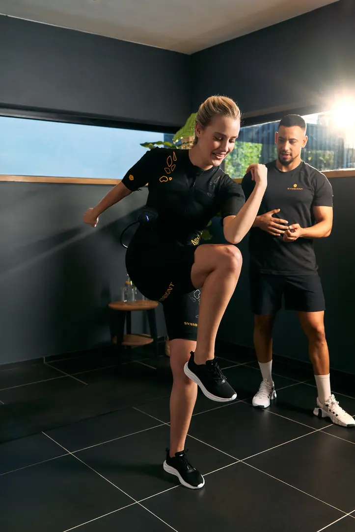 Vivi l’allenamento SYMBIONT EMS nel tuo studio EMS locale. Un personal trainer guida un cliente in una tuta SYMBIONT EMS durante una sessione di prova in uno studio EMS locale. Vivi un allenamento personalizzato, con supporto e motivazione nella tua prova EMS.